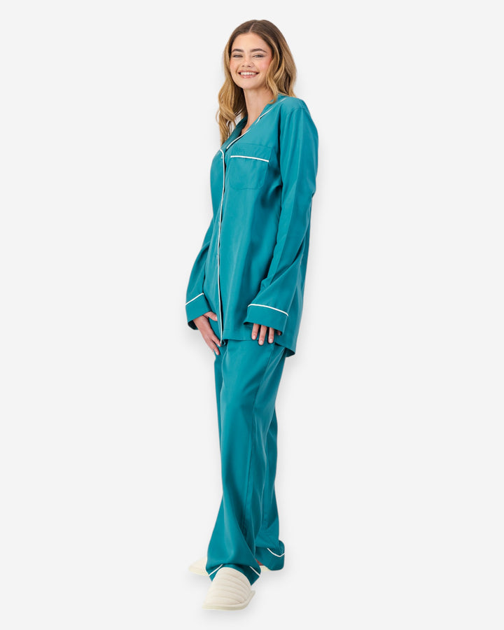 Woman wearing teal pyjamas with white piping on a white background