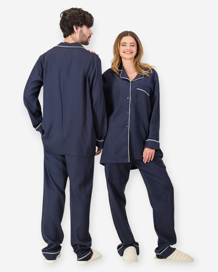 Two people wearing navy tencel pyjamas with white piping on a white background