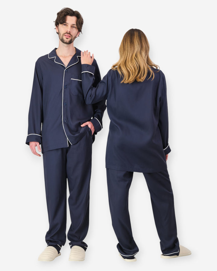 Two people wearing navy tencel pyjamas with white piping on a white background