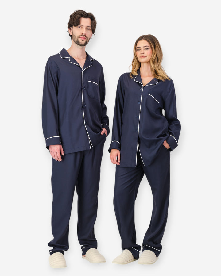 Two people wearing navy tencel pyjamas with white piping on a white background