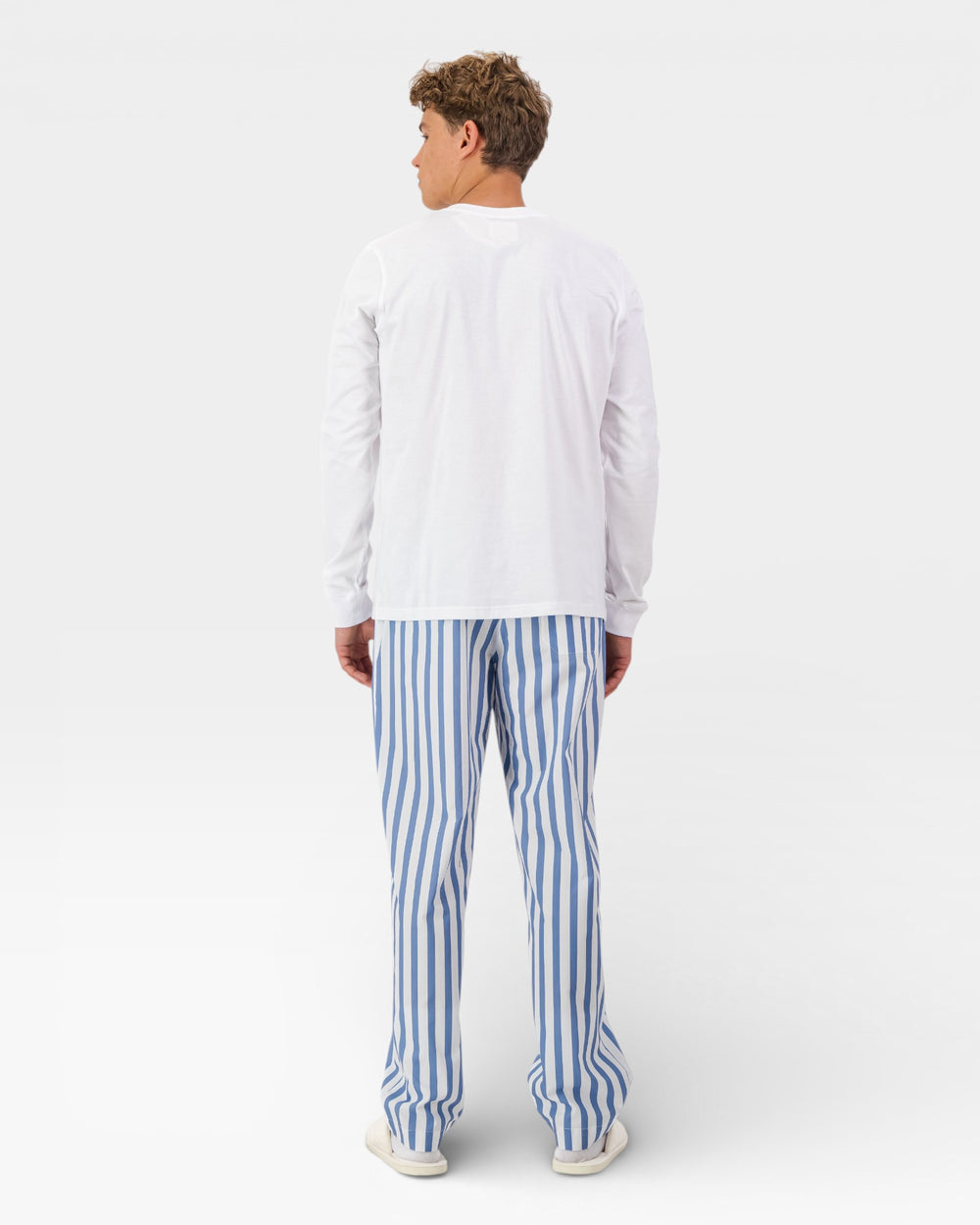 Man wearing a white long-sleeve shirt and blue striped pants on a white background