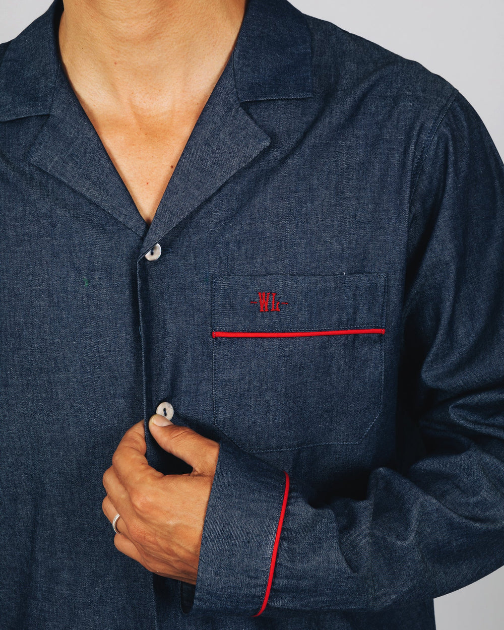 A close-up of a man wearing a dark blue denim pyjama shirt with red piping and a red embroidered 'W' on the chest pocket.