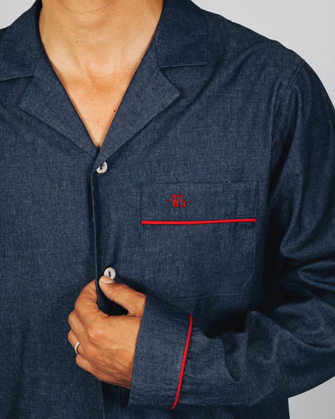 A close-up of a man wearing a dark blue denim pyjama shirt with red piping and a red embroidered 'W' on the chest pocket.