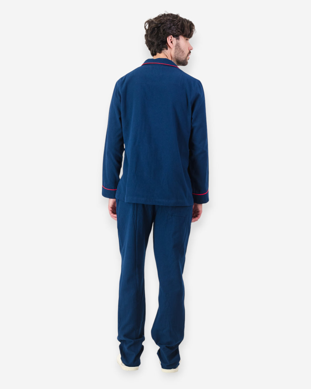 Man wearing navy blue flannel pyjamas with red piping on a white background