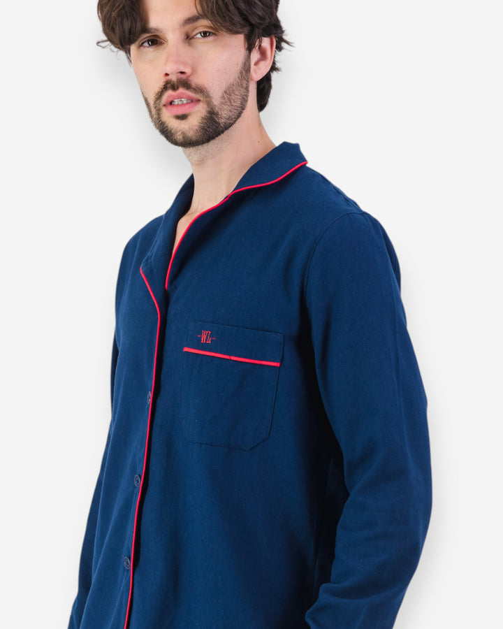 Man wearing navy blue flannel pyjamas with red piping on a white background