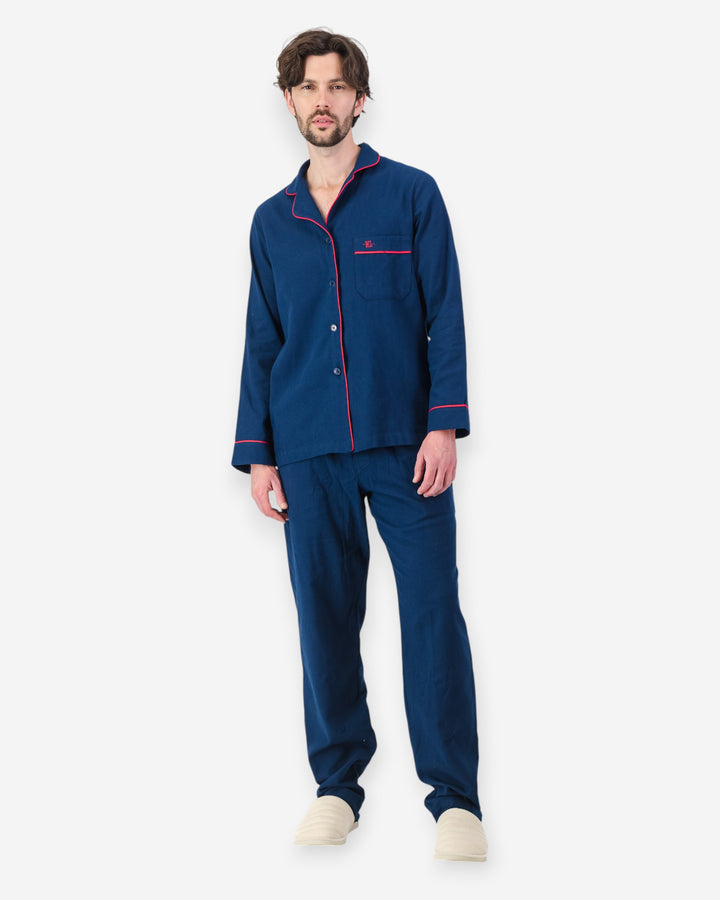 Man wearing navy blue flannel pyjamas with red piping on a white background
