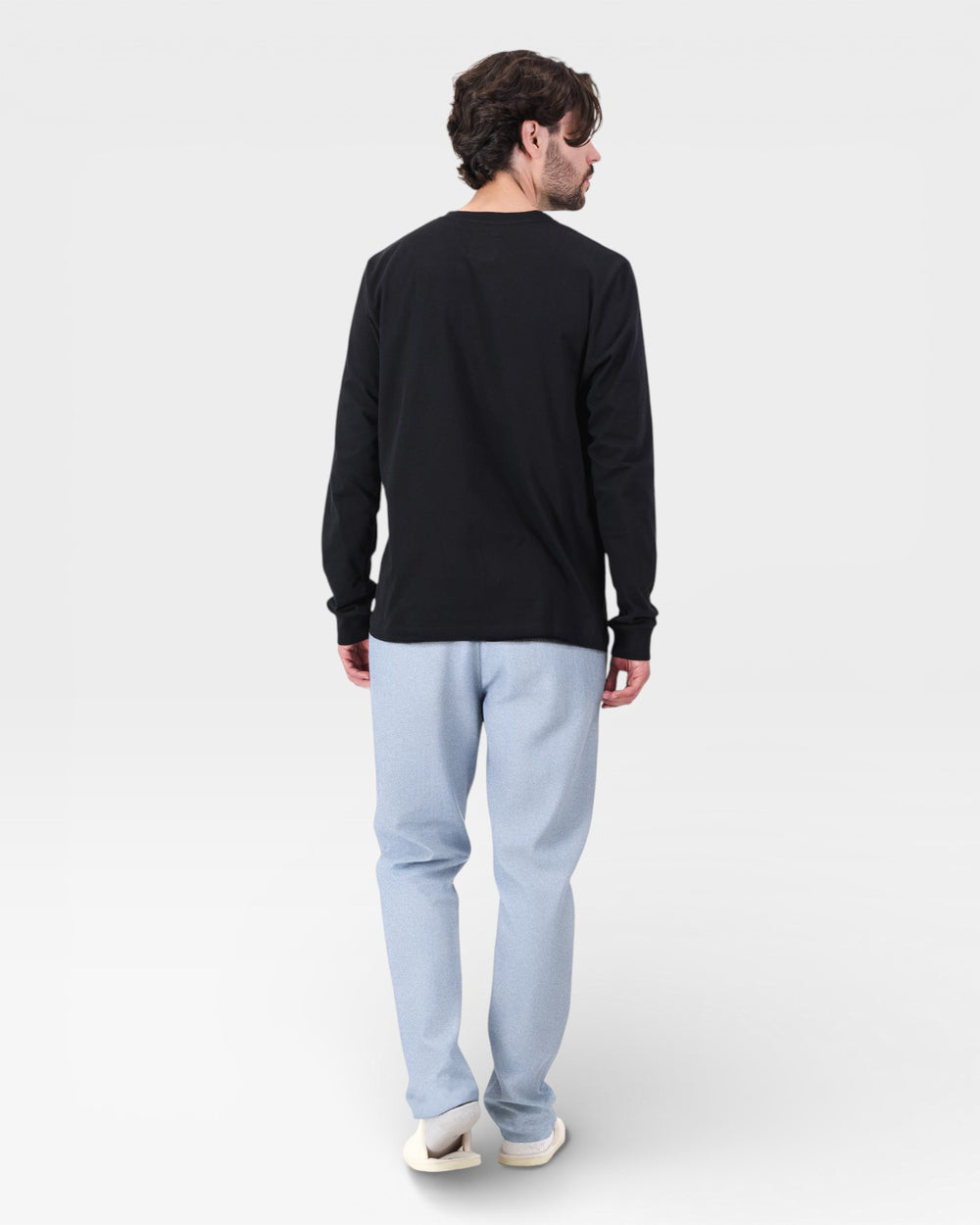 Person wearing a black long-sleeve shirt and light blue pants on a white background