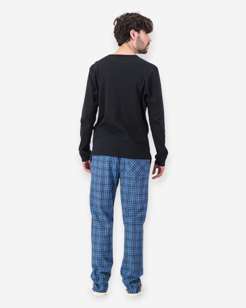 Man wearing a black long-sleeve shirt and blue plaid pajama pants on a white background