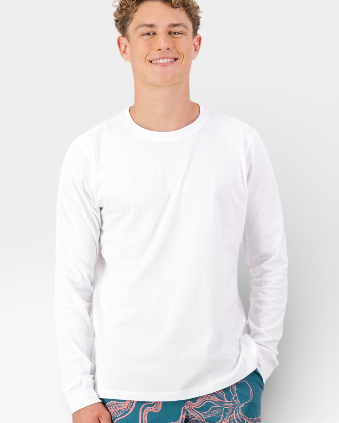 Man wearing a white long-sleeve shirt with colorful pants on a plain background