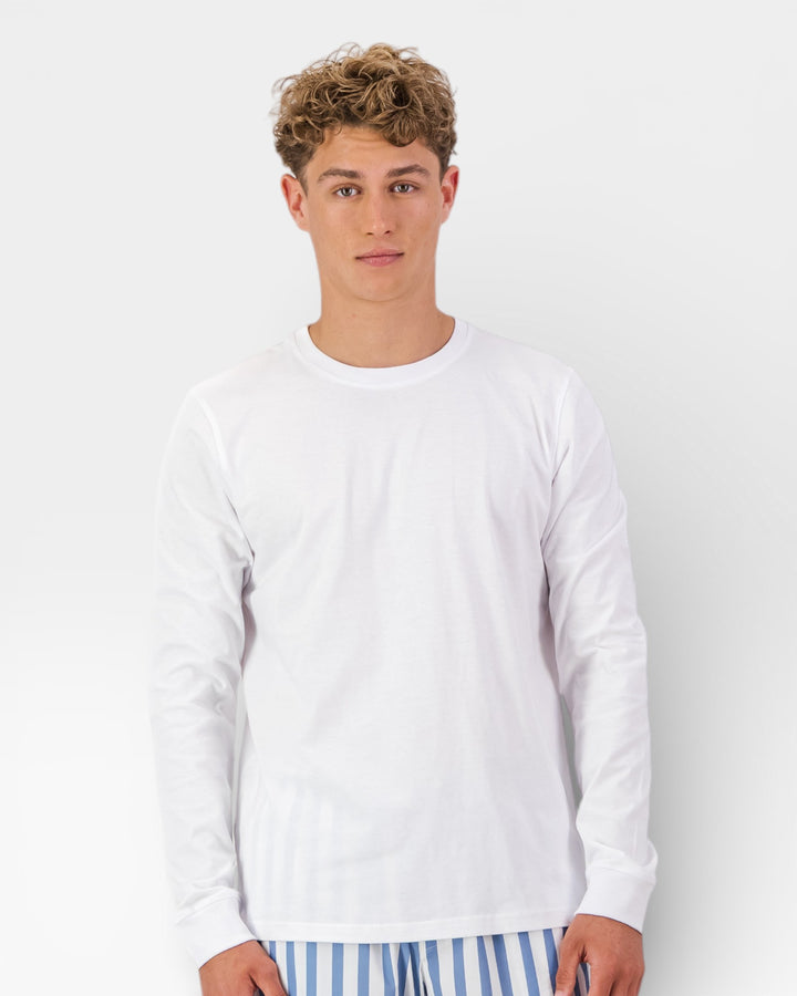 Man wearing a white long-sleeve shirt and striped pajama pants on a plain background