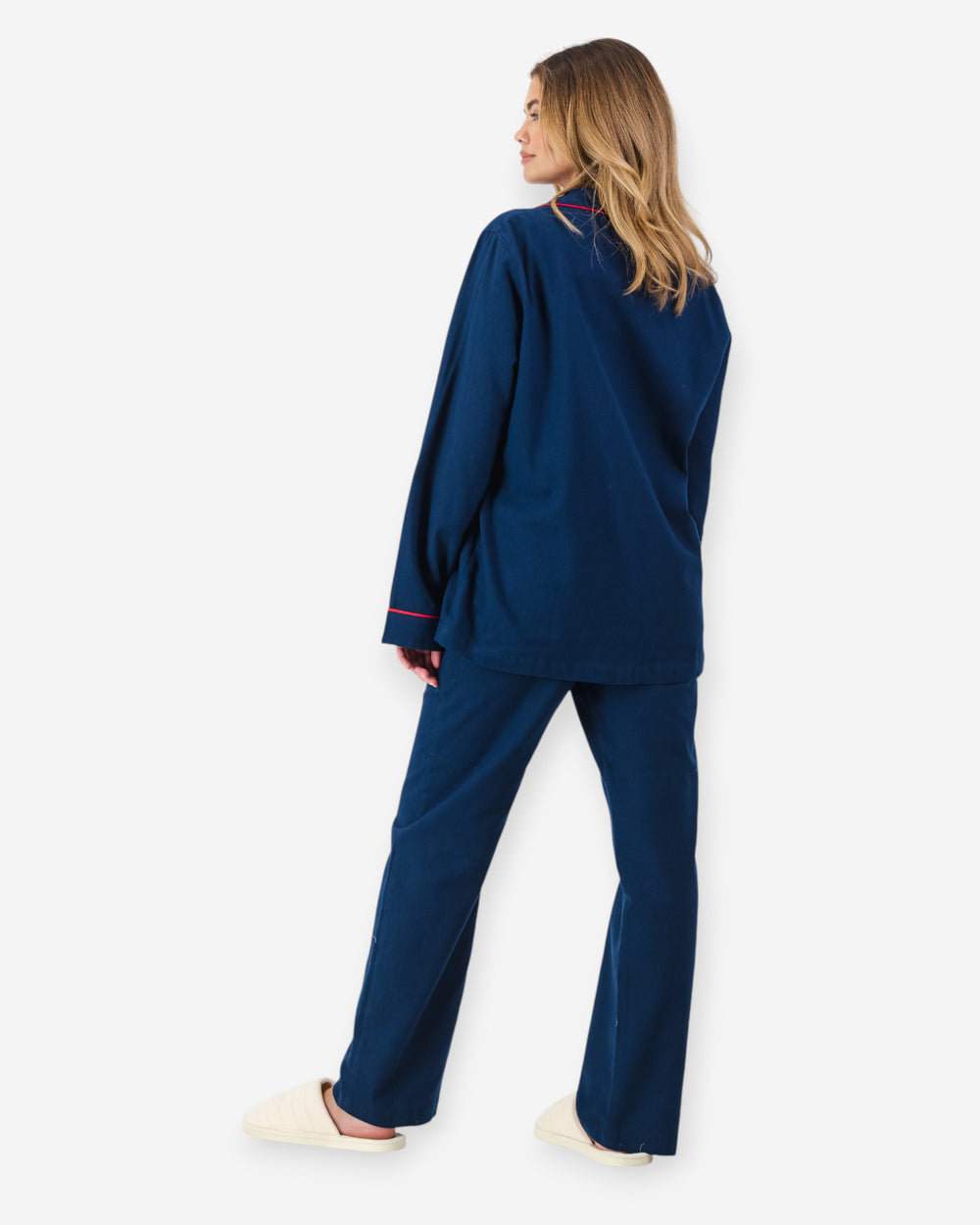 Woman wearing a navy blue flannel pyjama set with red piping on a white background