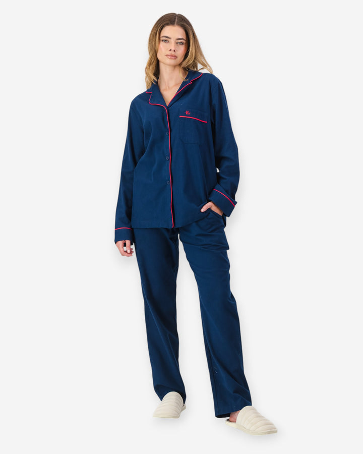 Woman wearing a navy blue flannel pyjama set with red piping on a white background